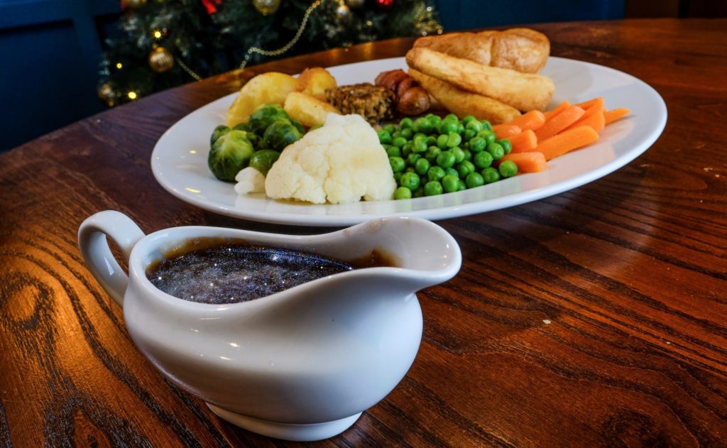 A gravy boat filled with glittery gravy next to a Christmas dinner