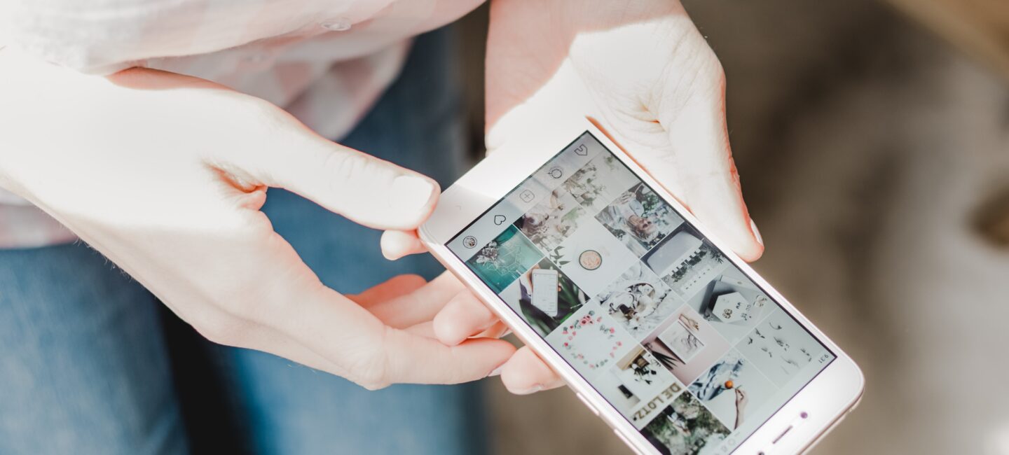 Picture of a woman's hands holding a phone displaying an Instagram grid
