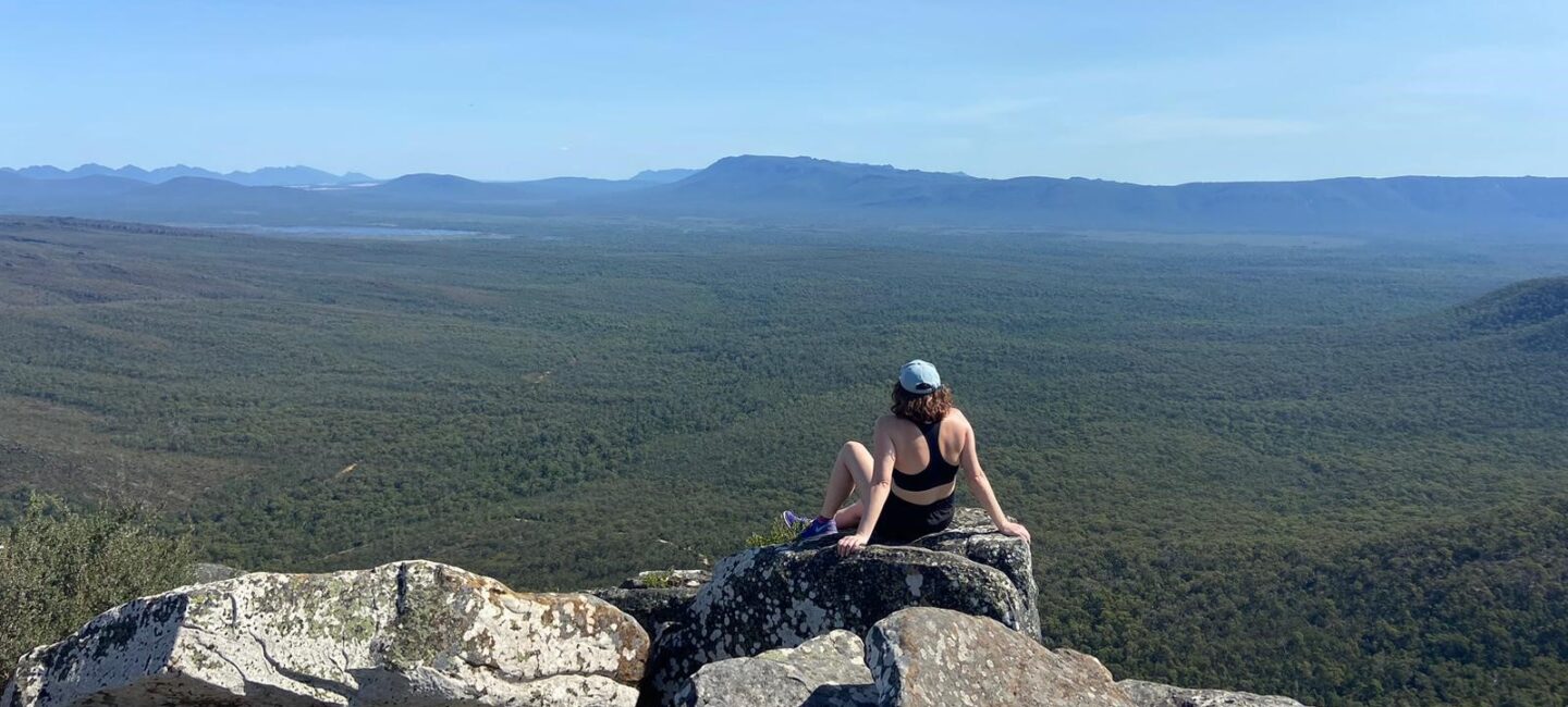 Georgie sitting in the sunshine on a rock looking out at a view in New Zealand