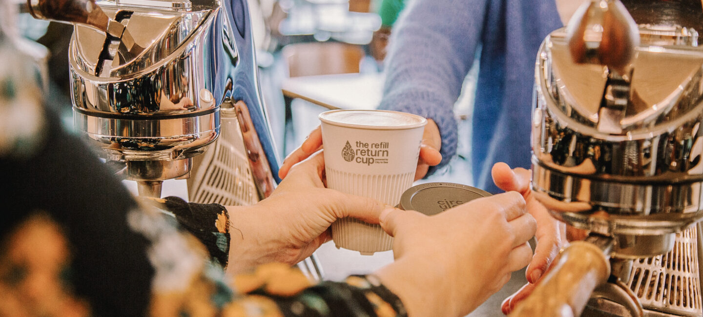 A hand passing a reusable cup over a counter in a coffee shop