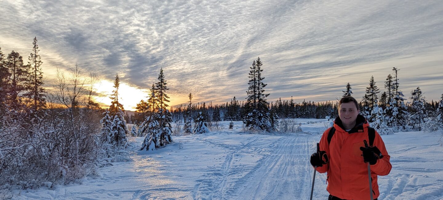 Nick on cross country skis in front of a snowy backdrop as the sun sets