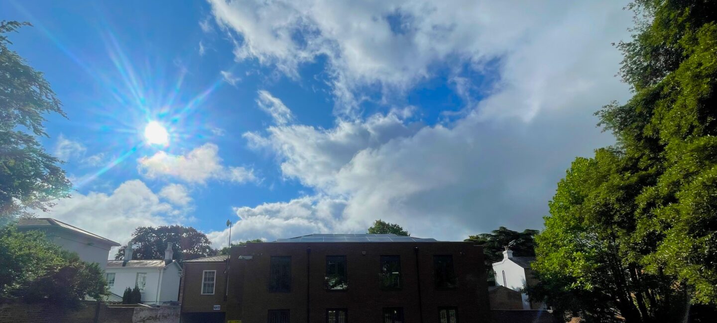 The roof of WPR's office with solar panels with the sun and blue sky behind it