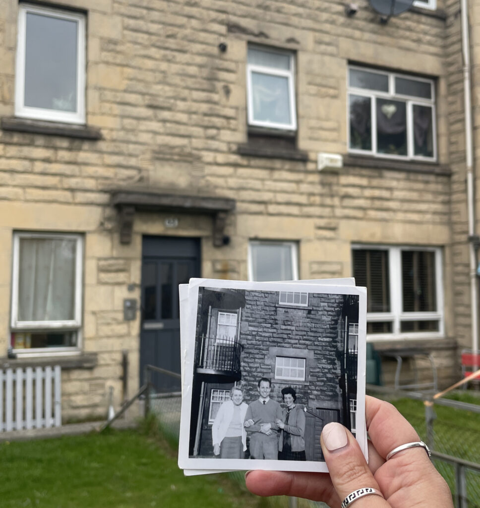 Old black and white photograph of a building being held up in front of the same building in current times