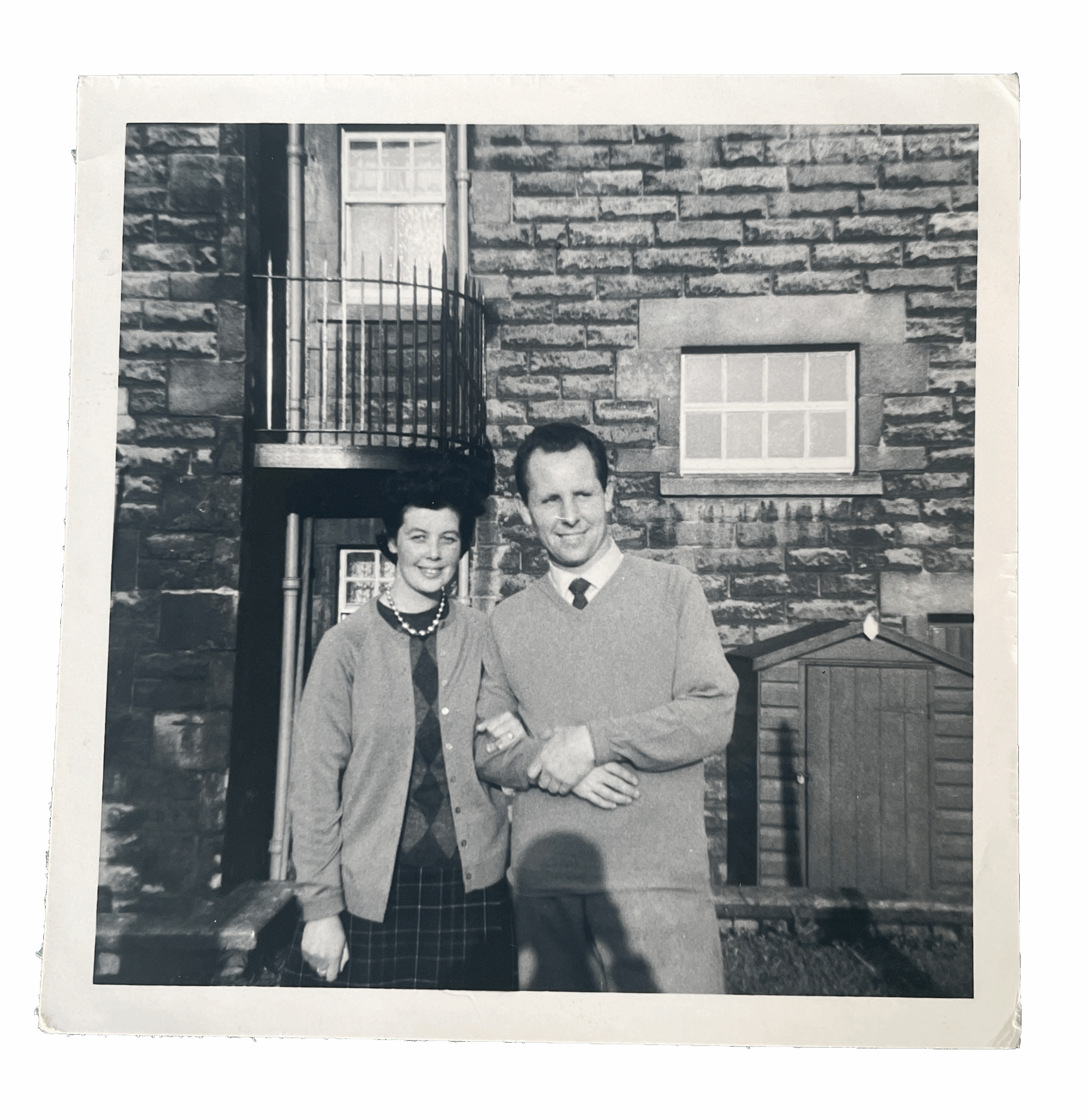 Old black and white image of a man and woman standing in front of a house