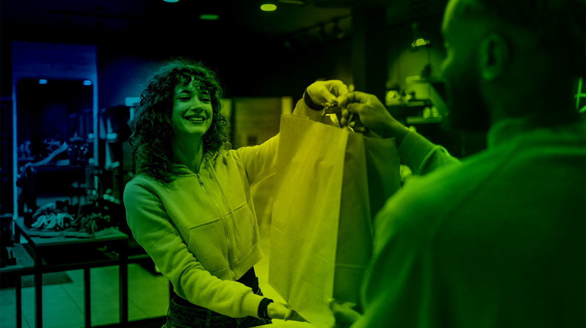 A smiling woman being handed a bag by a shop assistant