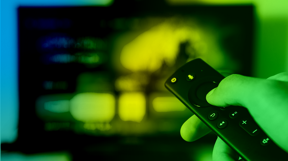 A hand holding a remote control and pointing it at a TV